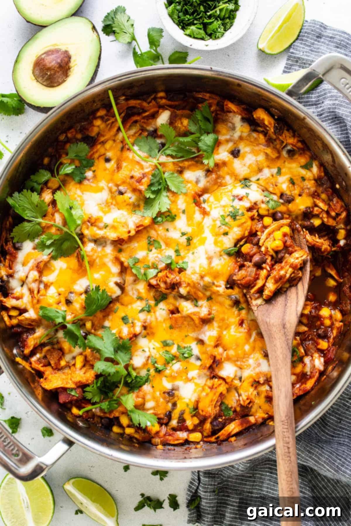 A close-up of the bubbling Mexican chicken enchilada skillet, fresh out of the oven, with a wooden spoon scooping a portion.