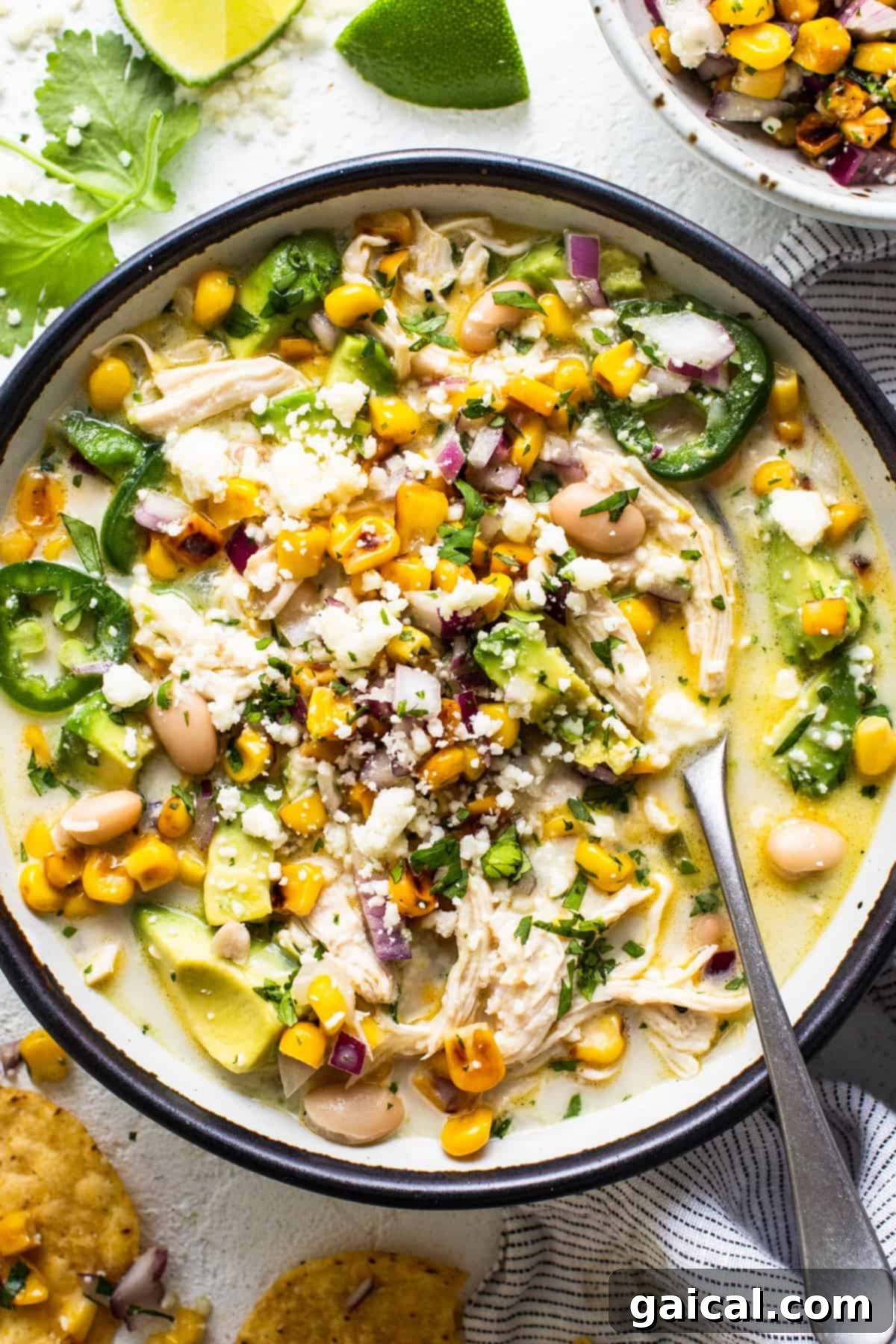 A generously sized, inviting bowl of Street Corn Chicken Chili, perfectly served with a side of crispy golden tortilla chips, a fresh lime wedge, and a sprinkle of cilantro. A comforting and satisfying meal ready to be savored.