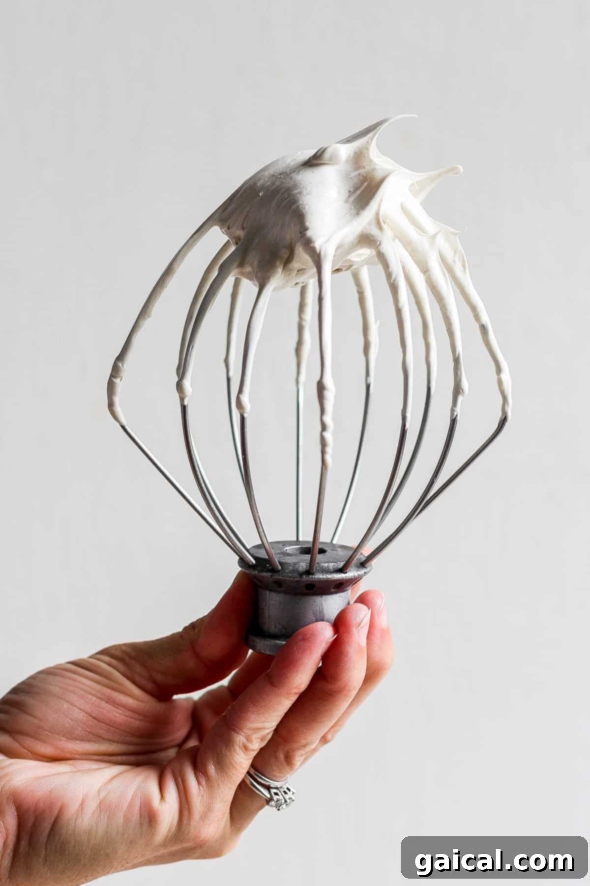 A person holding a whisk with fluffy whipped brown sugar Swiss meringue in it, ready to top a dessert.