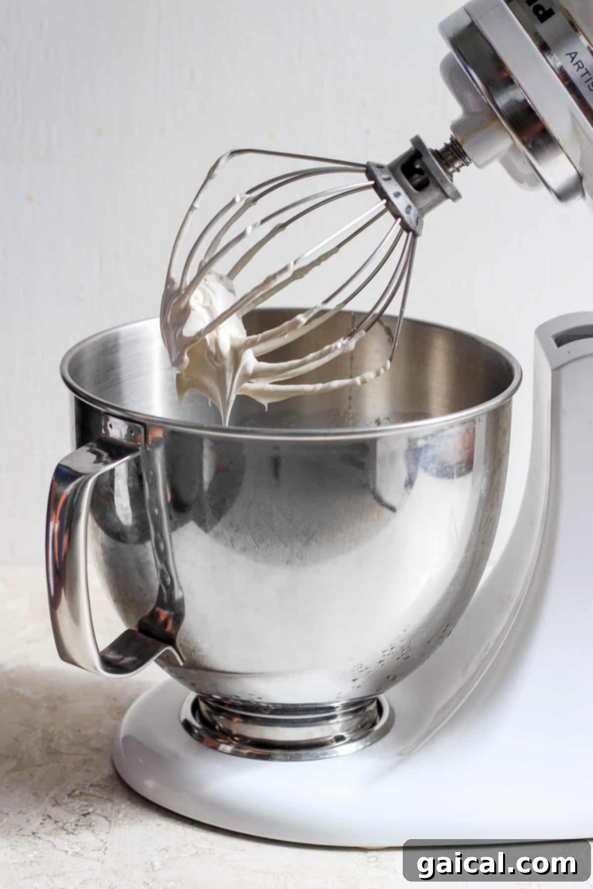 A white stand mixer with a whisk attachment, preparing to whip the brown sugar Swiss meringue.