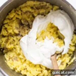A bowl of mashed potatoes being mixed with whipped cottage cheese and milk.