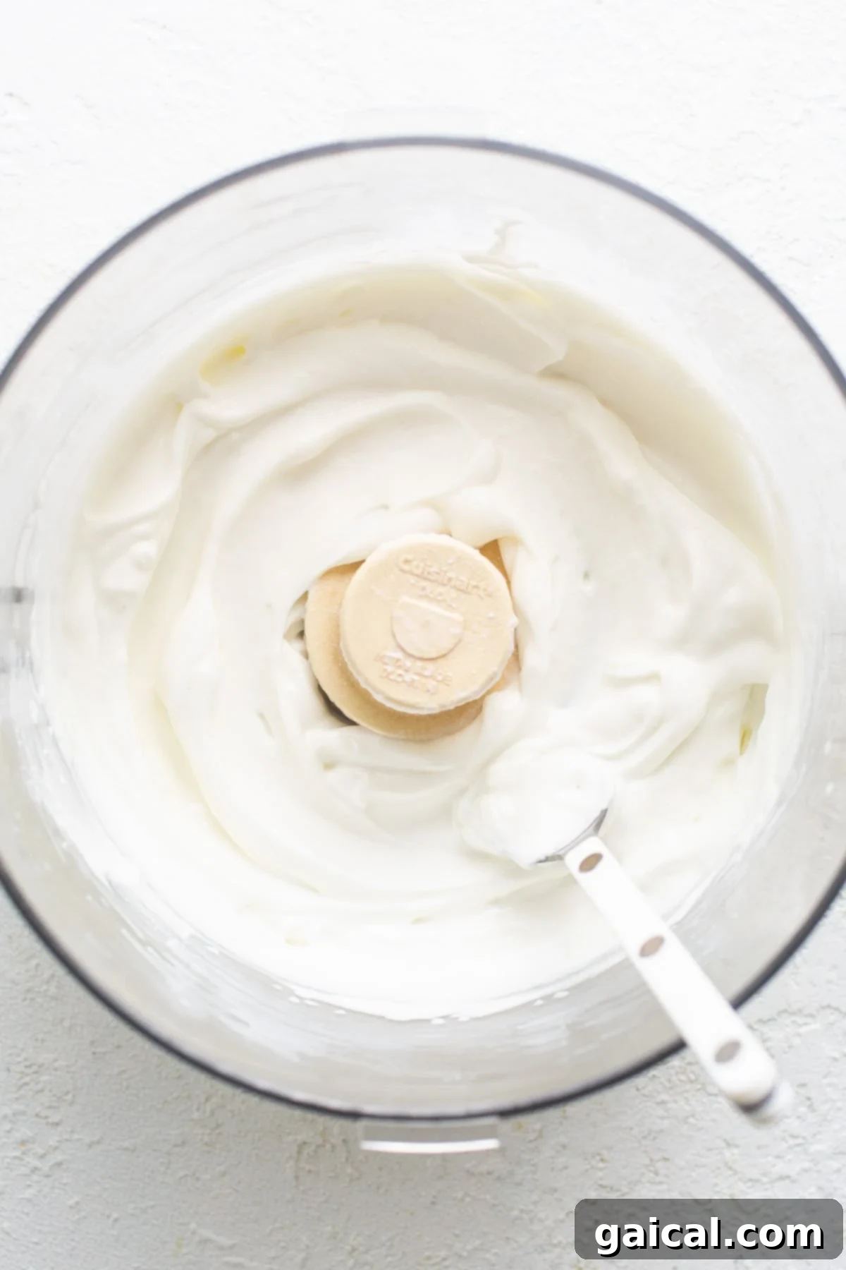 A close-up of a blender or food processor bowl, containing creamy whipped cottage cheese ready to be incorporated into the potatoes.