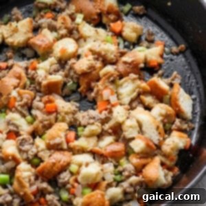 A skillet filled with savory stuffing, bread cubes, herbs, and vegetables.