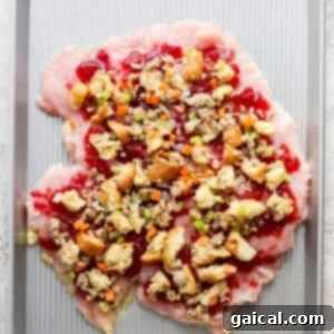 A butterflied turkey breast on a baking sheet, layered with cranberry sauce and savory stuffing.
