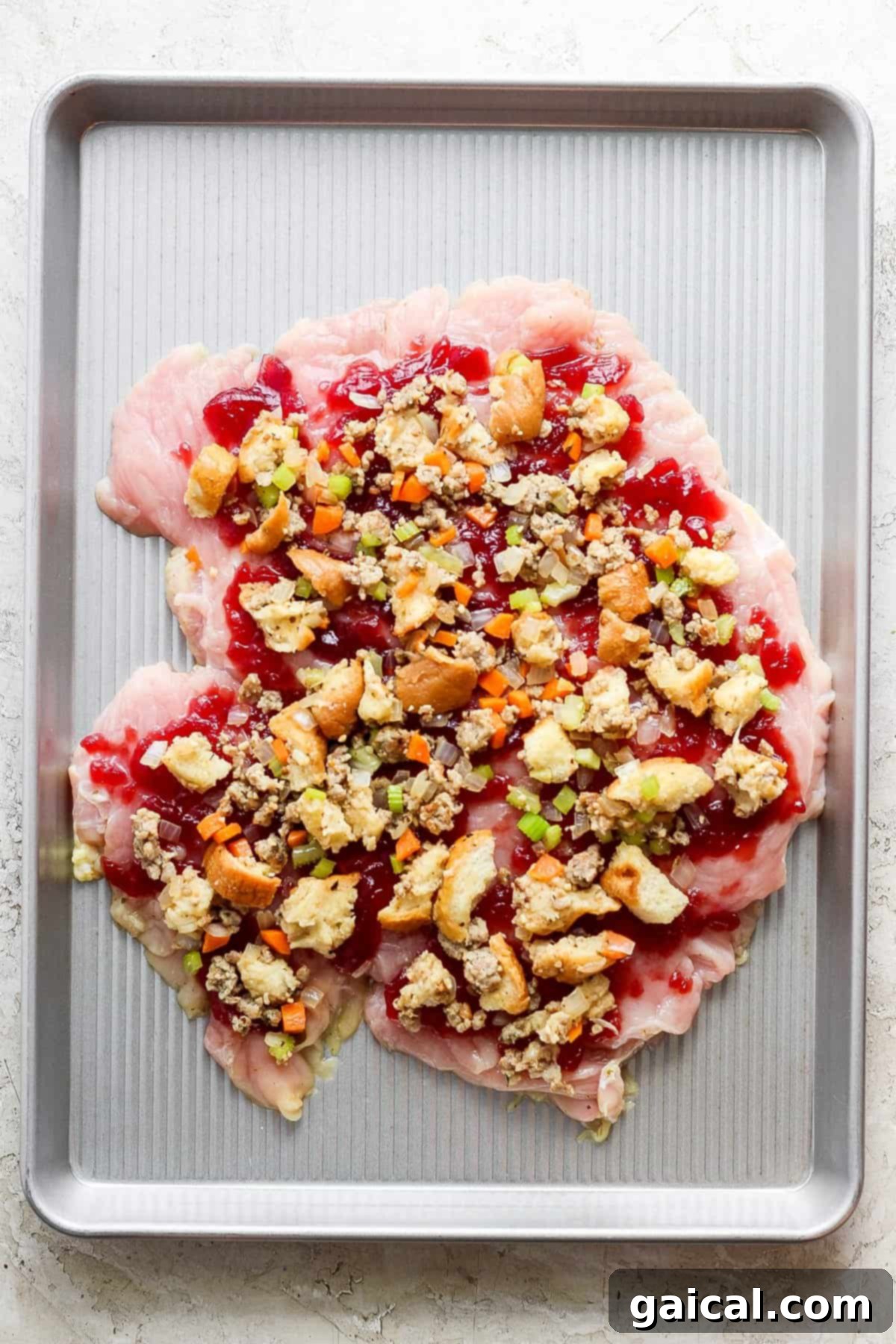 Festive Turkey Roulade with Hearty Italian Sausage Stuffing 5 A baking sheet with a neatly rolled turkey roulade, topped with a vibrant cranberry mixture, ready for the oven.