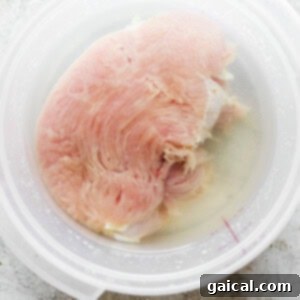 A bowl of turkey breast submerged in brining liquid.