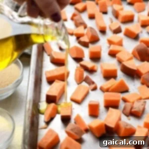 Drizzling olive oil onto sweet potato cubes on a baking sheet.