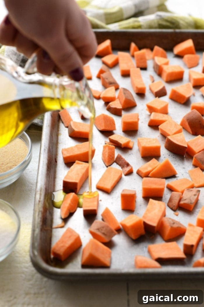 Cubed raw sweet potatoes drizzled with olive oil and spices on a baking sheet, ready for roasting.