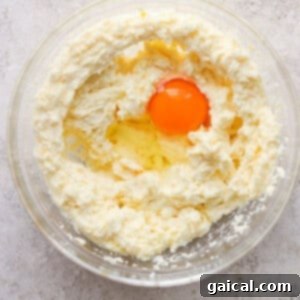 A single egg added to the wet ingredients in a mixing bowl, ready to be gently beaten into the cookie dough.