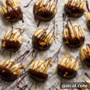 Close-up of chocolate-dipped cookies with fresh orange zest sprinkled on top, arranged on parchment paper.