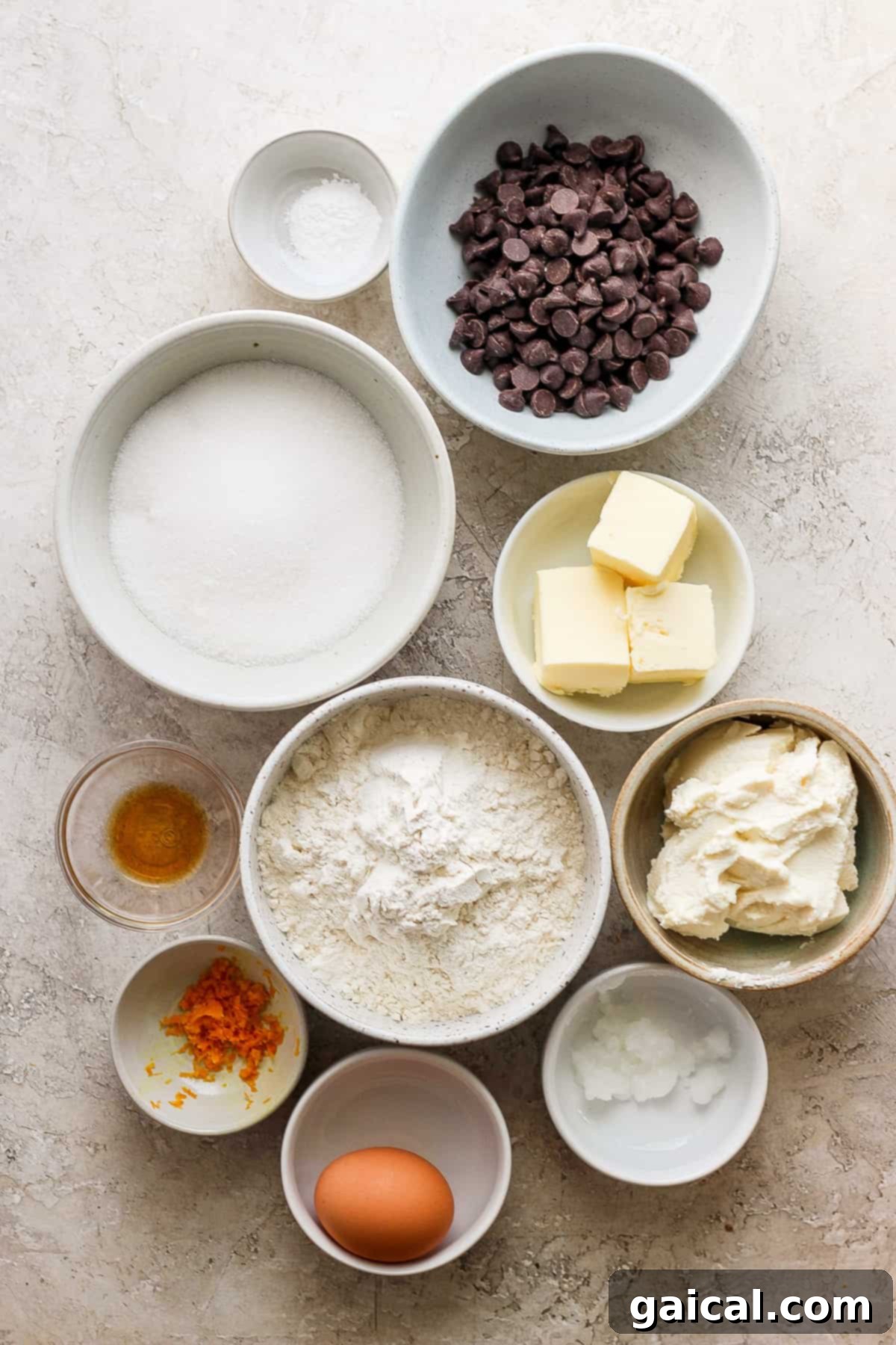 A collection of fresh ingredients for baking cookies, including oranges, a bowl of ricotta, flour, and chocolate, arranged on a rustic wooden table.