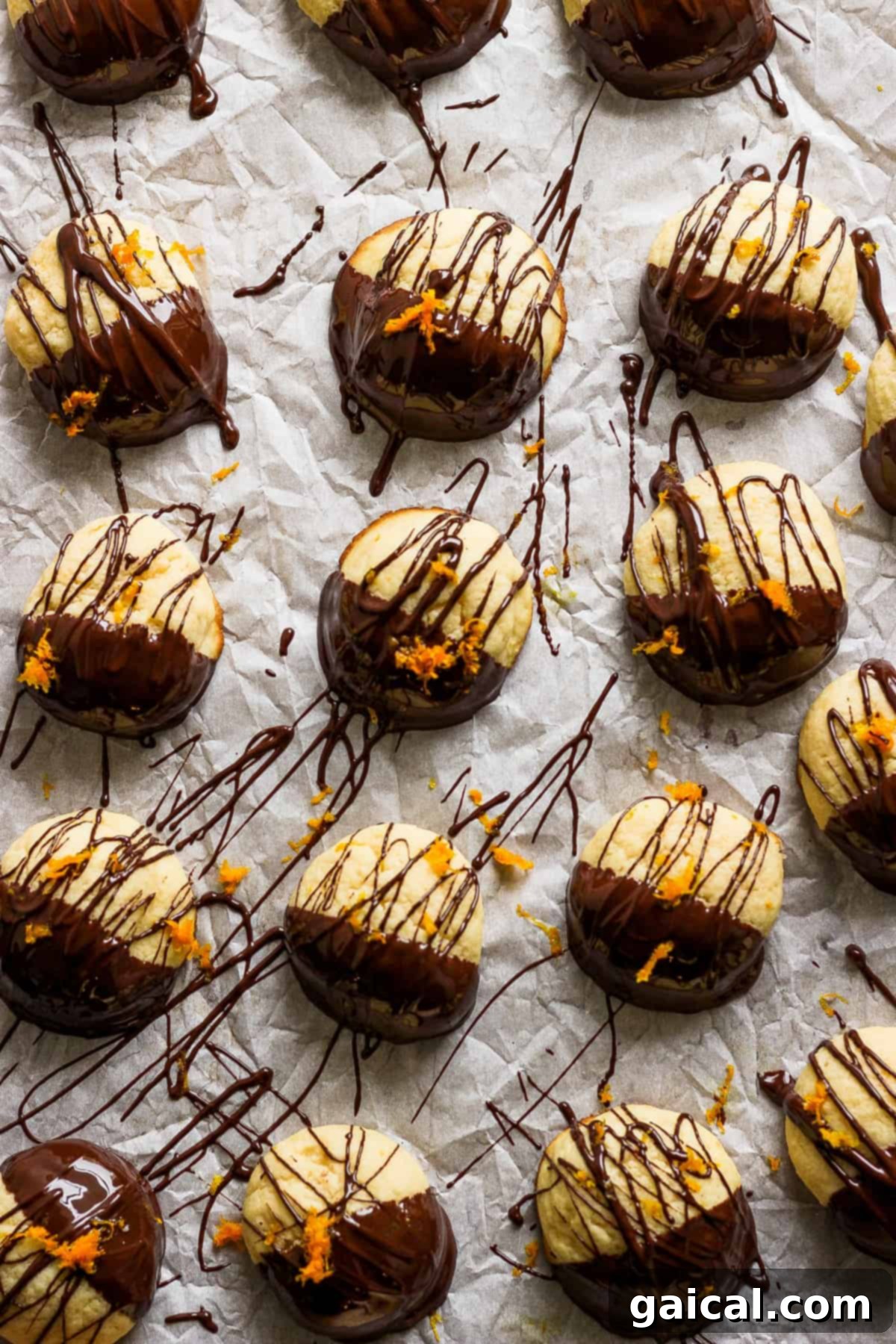 A beautifully arranged stack of chocolate-dipped ricotta cookies, garnished with orange zest, presented on parchment paper.