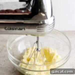 A person creaming butter and sugar together in a bowl using a hand mixer, aiming for a light and fluffy consistency.