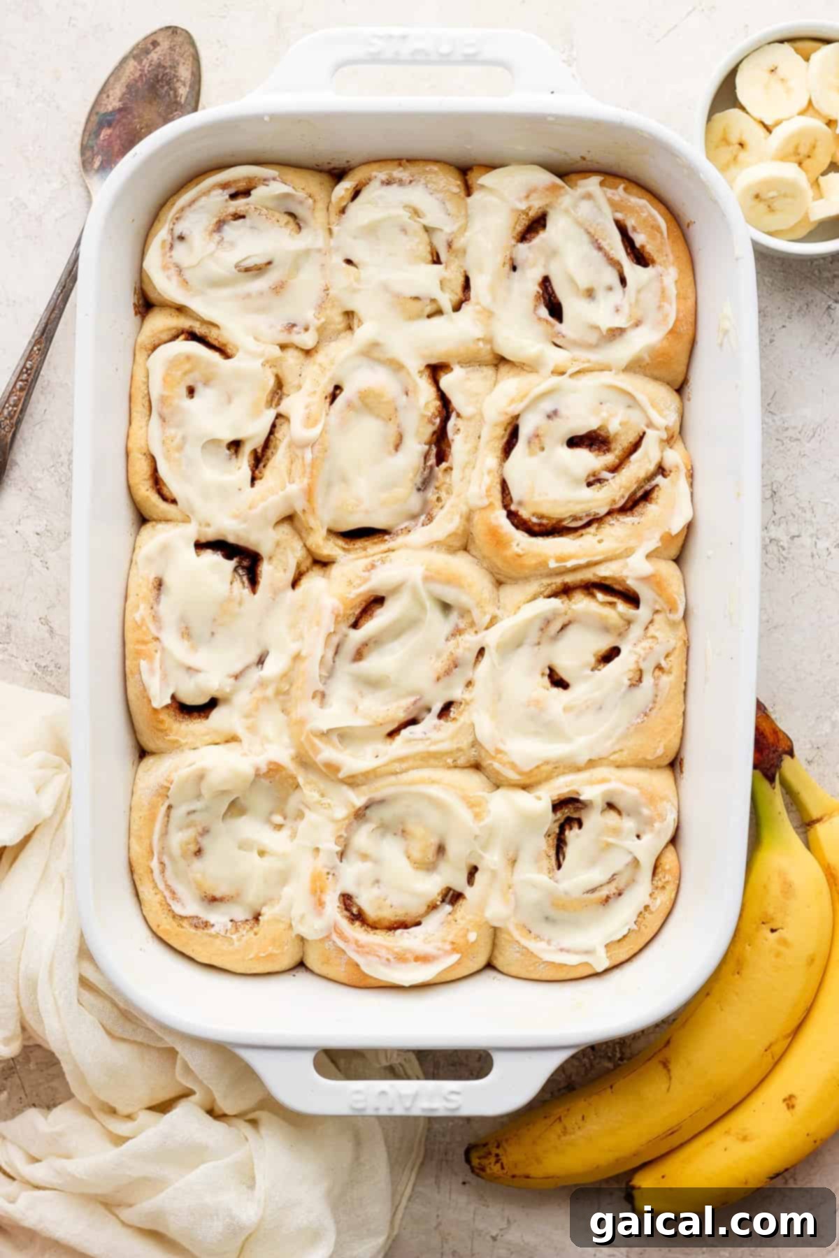 Nutty Brown Butter Banana Bread Cinnamon Rolls 2 Freshly baked brown butter banana bread cinnamon rolls in a baking dish, garnished with banana slices.