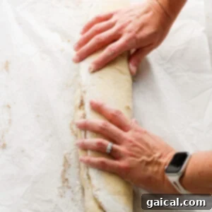 Nutty Brown Butter Banana Bread Cinnamon Rolls 11 A person's hands carefully slicing a rolled log of cinnamon roll dough into individual rolls.