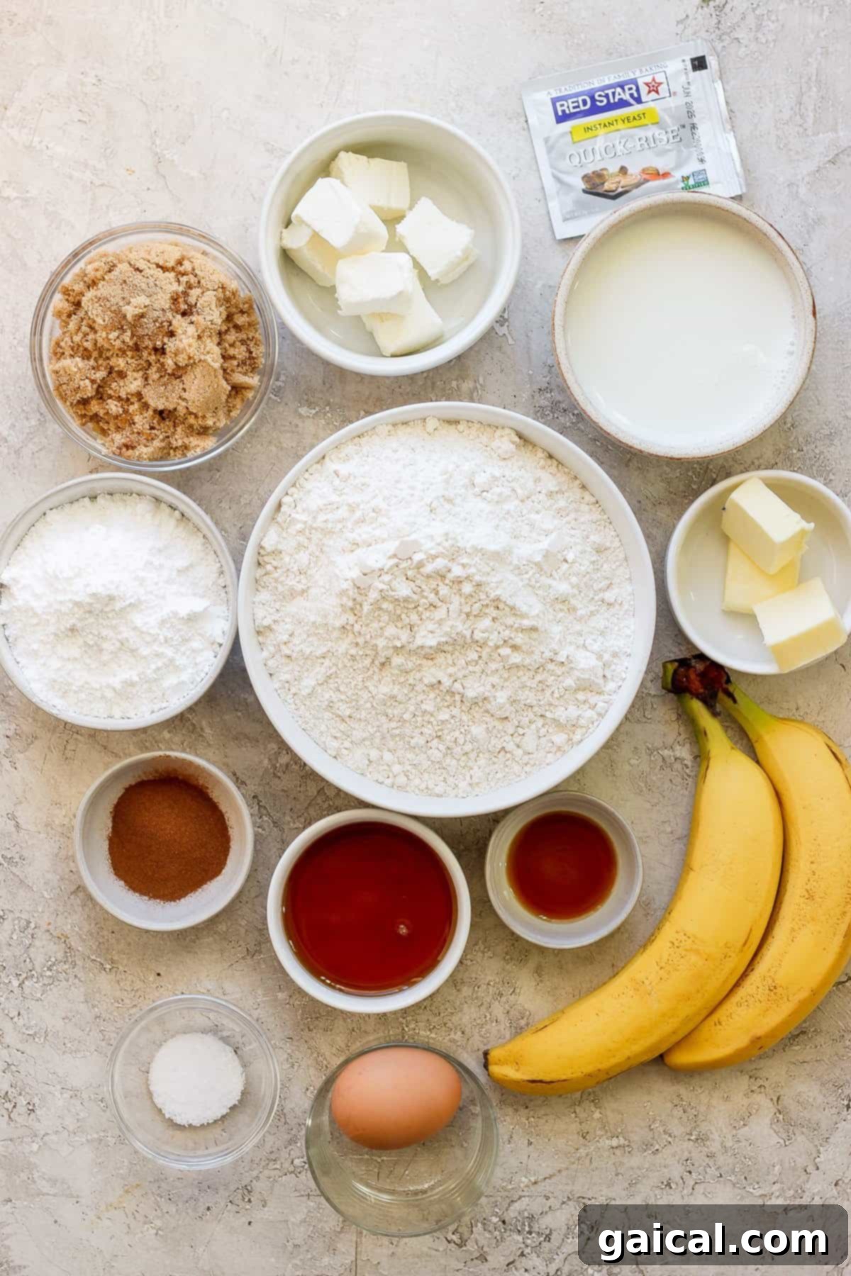 Nutty Brown Butter Banana Bread Cinnamon Rolls 3 A vibrant display of banana bread ingredients arranged on a rustic wooden table, including bananas, flour, butter, and spices.
