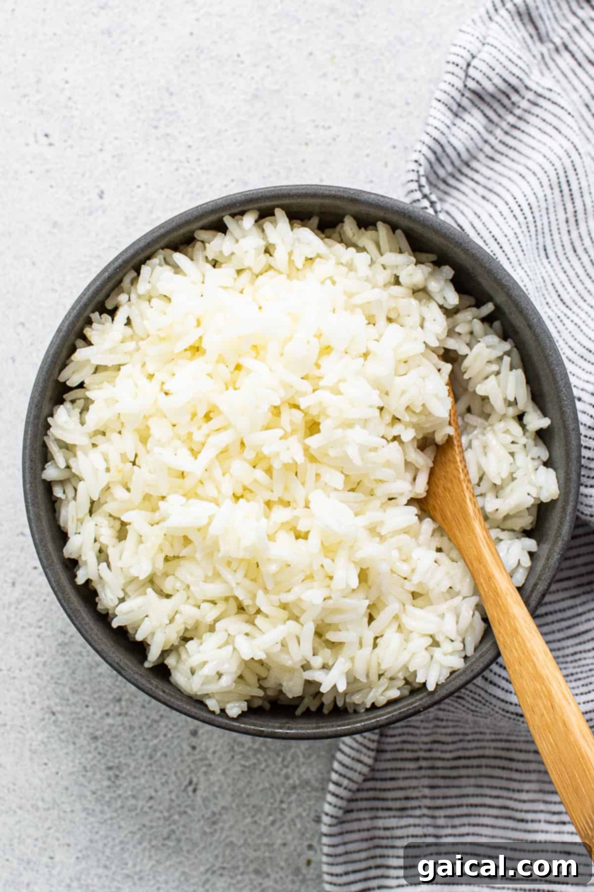 White rice in a bowl with a wooden spoon, ready to be served.