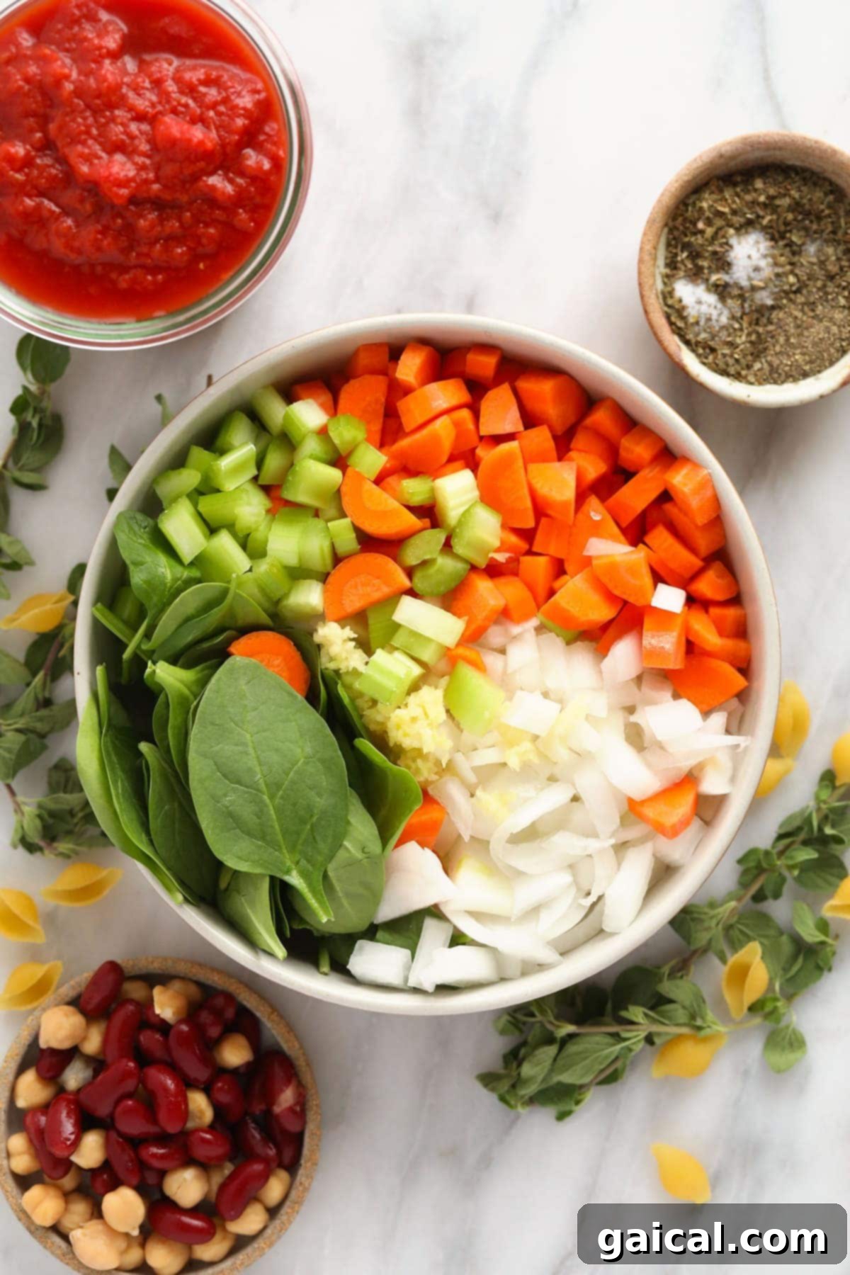 Make this vegetable packed minestrone soup and eat it all week long! A vibrant bowl filled with fresh, uncooked minestrone soup ingredients: carrots, celery, onion, garlic, and spinach, ready for preparation.