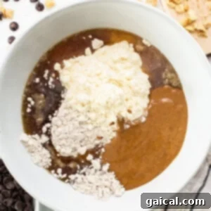 A white bowl with ingredients for a peanut butter chocolate chip cookie dough, illustrating the mixing process for the nougat layer.