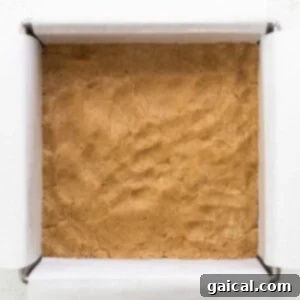 A brownie-like base pressed firmly into a square baking dish, showing the smoothed nougat layer ready for the next step.