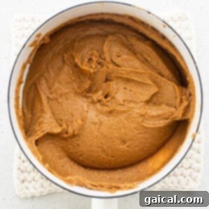 A rich peanut butter caramel mixture in a pan with a wooden spoon, before the addition of crunchy peanuts.