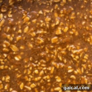 A baking dish filled with distinct, visible layers of oat base and peanut butter caramel with nuts, ready for freezing.