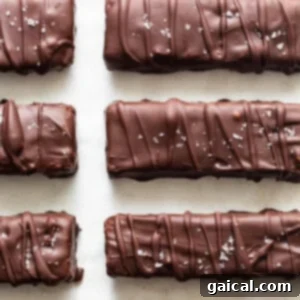 A lineup of chocolate-covered bars resting on a clean white surface, awaiting final setting in the freezer to achieve perfect texture.