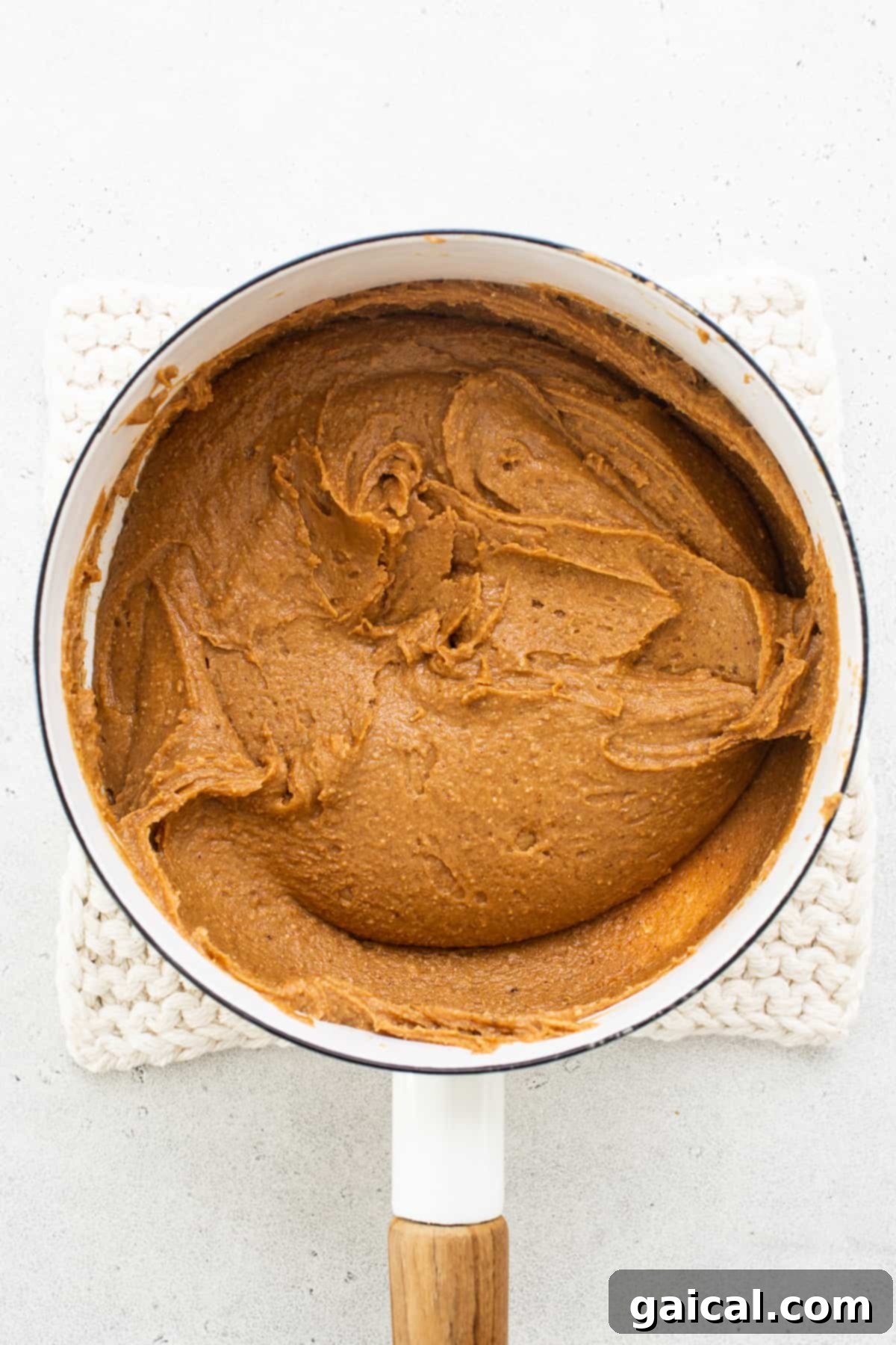 A close-up of a rich, thick caramel sauce simmering in a pan with a wooden spoon, ready to be spread as a layer.