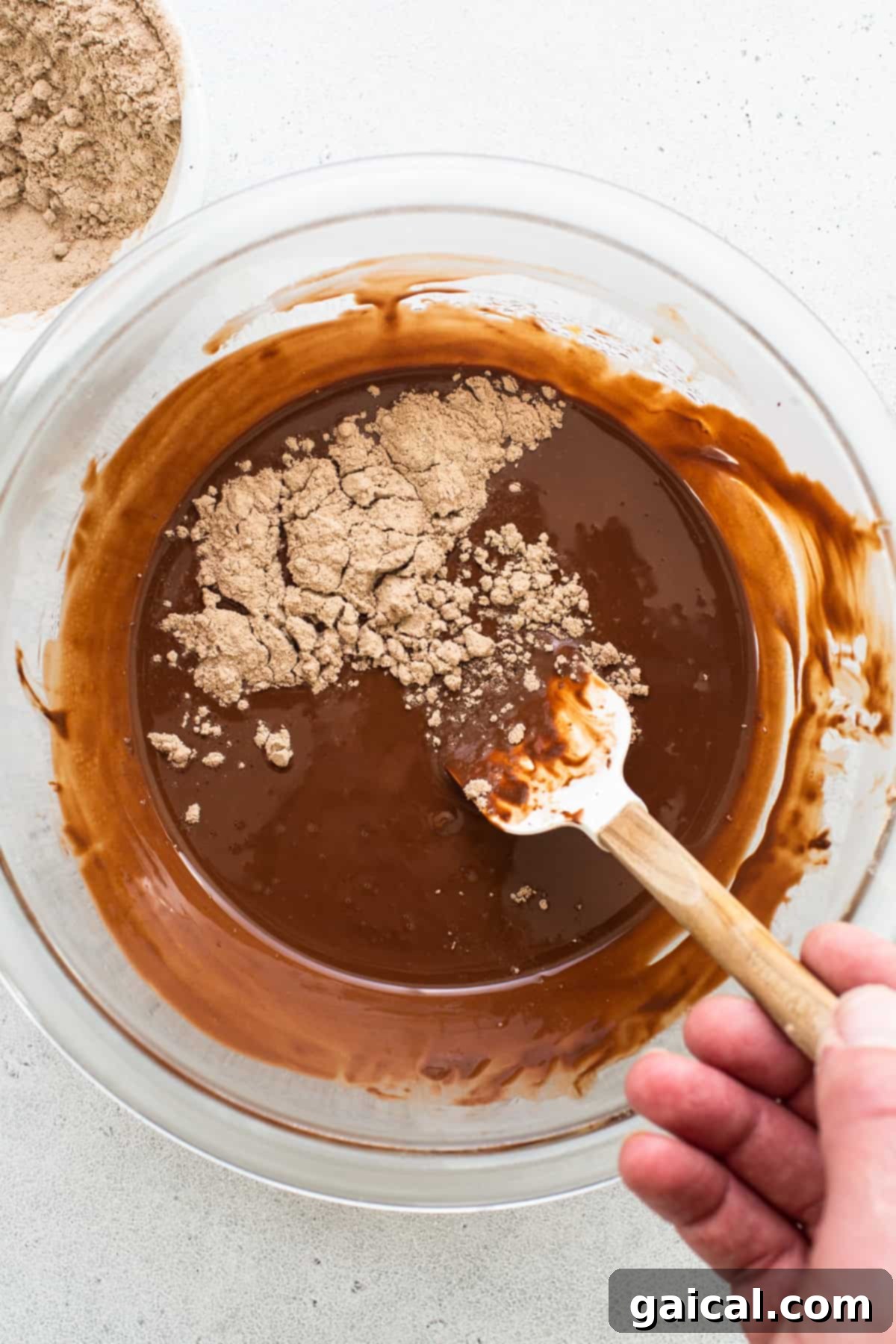 Protein-Powered Peanut Butter Chocolate Crisps 5 Hands stirring melted chocolate in a bowl with a wooden spoon, showcasing the smooth, glossy texture.