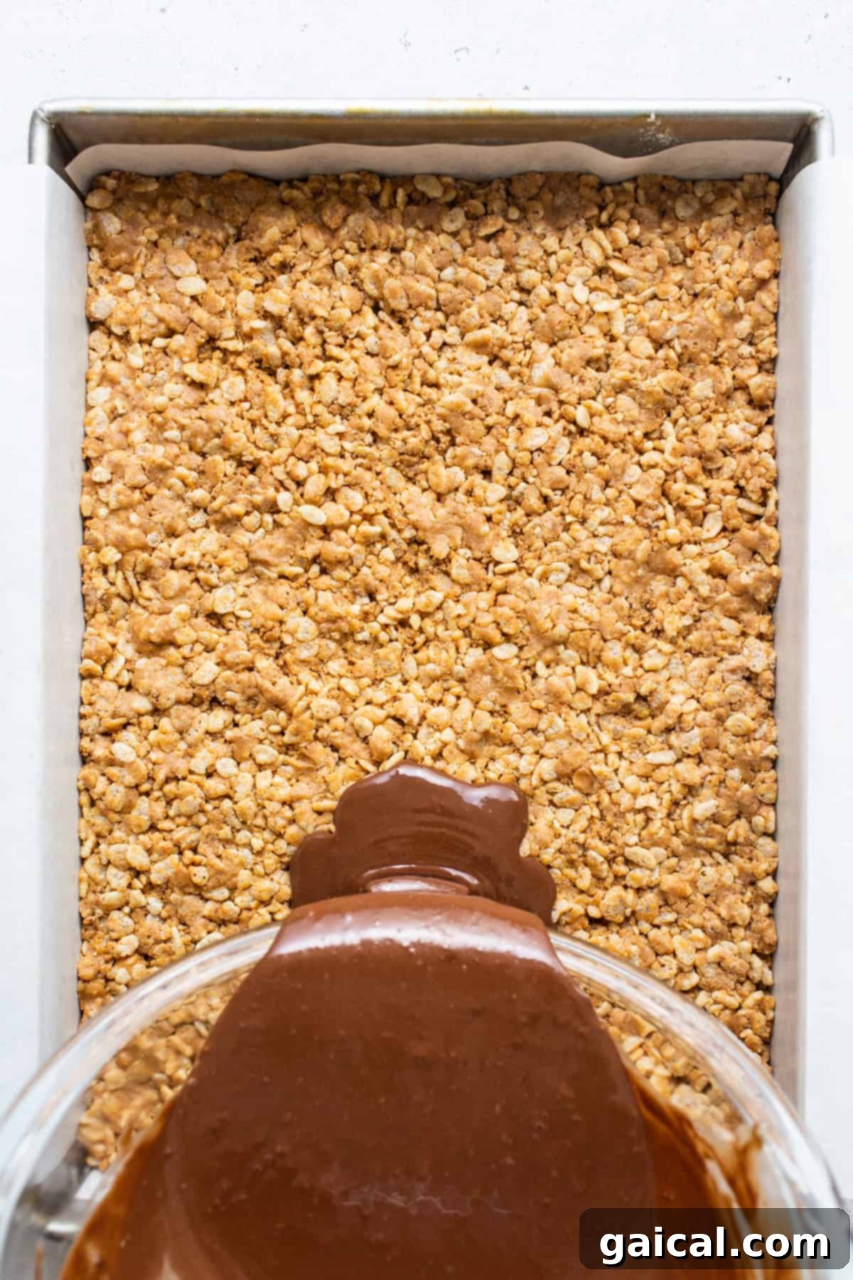 Protein-Powered Peanut Butter Chocolate Crisps 6 A rich chocolate sauce being smoothly poured over a layer of crispy oats in a baking dish, creating the final layer.