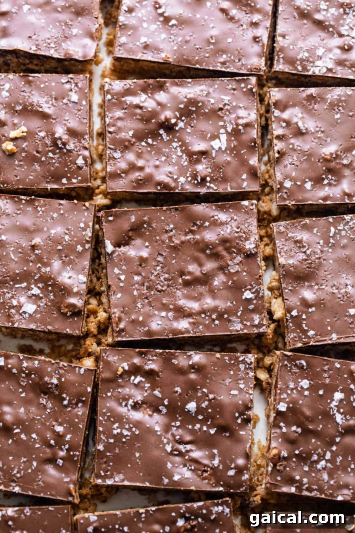 Protein-Powered Peanut Butter Chocolate Crisps 7 A close-up shot of perfectly squared chocolate protein bars with a slight sprinkle of sea salt on a white plate, highlighting their appetizing texture.