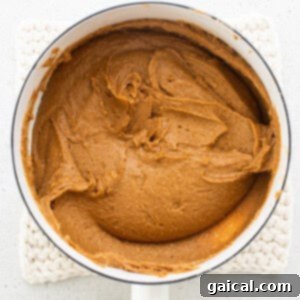 Pumpkin butter melting in a pan with a wooden spoon, illustrating the initial melting process.