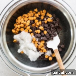 Chocolate chips in a bowl with a wooden spoon, being stirred gently over a double boiler.
