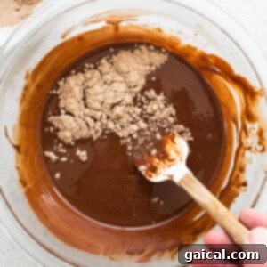 A person mixing chocolate in a bowl with a wooden spoon, incorporating protein powder into the melted mixture.