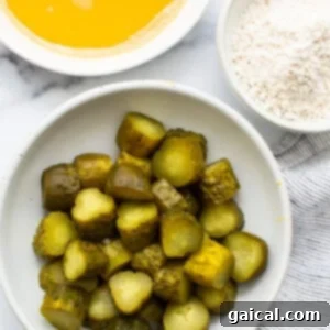 A bowl of sliced dill pickles next to a bowl of all-purpose flour and another bowl of panko breadcrumbs, meticulously prepared for the breading process.