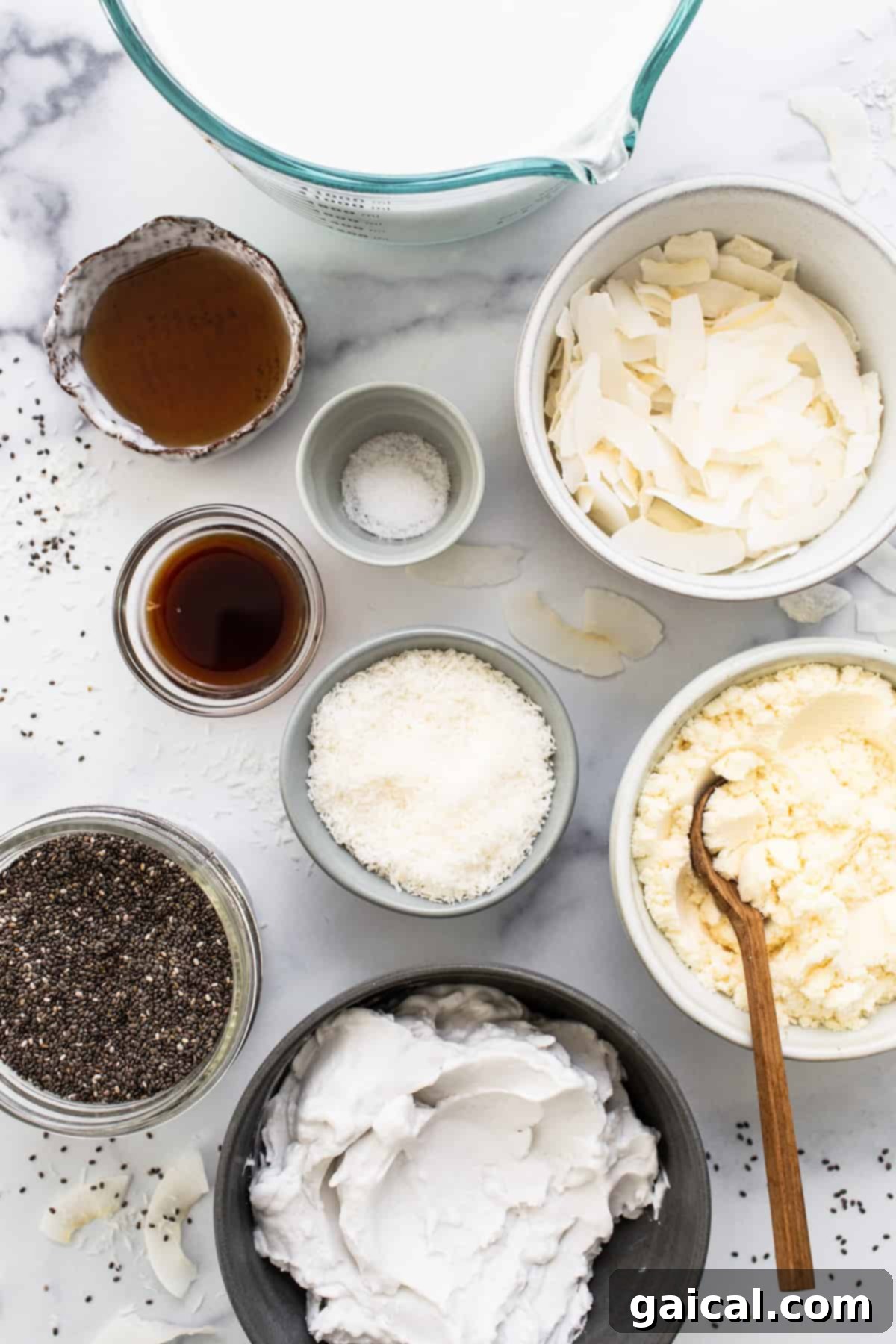 Dreamy Protein Coconut Cream Pie Chia Pudding 3 All the individual ingredients for a chia pudding recipe laid out in small bowls on a marble table, ready for preparation.