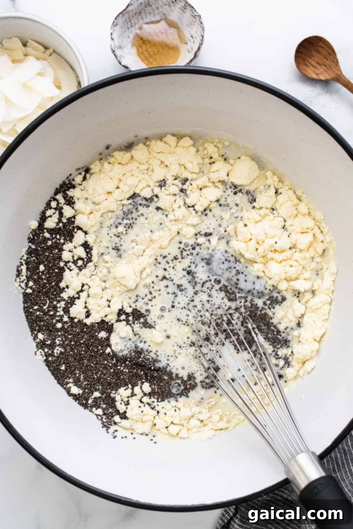 Dreamy Protein Coconut Cream Pie Chia Pudding 4 A bowl filled with mixed ingredients, likely the chia pudding mixture, in a pan with a wooden spoon resting inside, ready to be whisked.