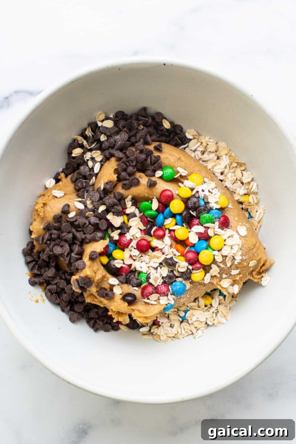 Epic Protein Cookie Dough 6 A white bowl filled with rolled oats, granola, and mini chocolate chips, illustrating ingredients.