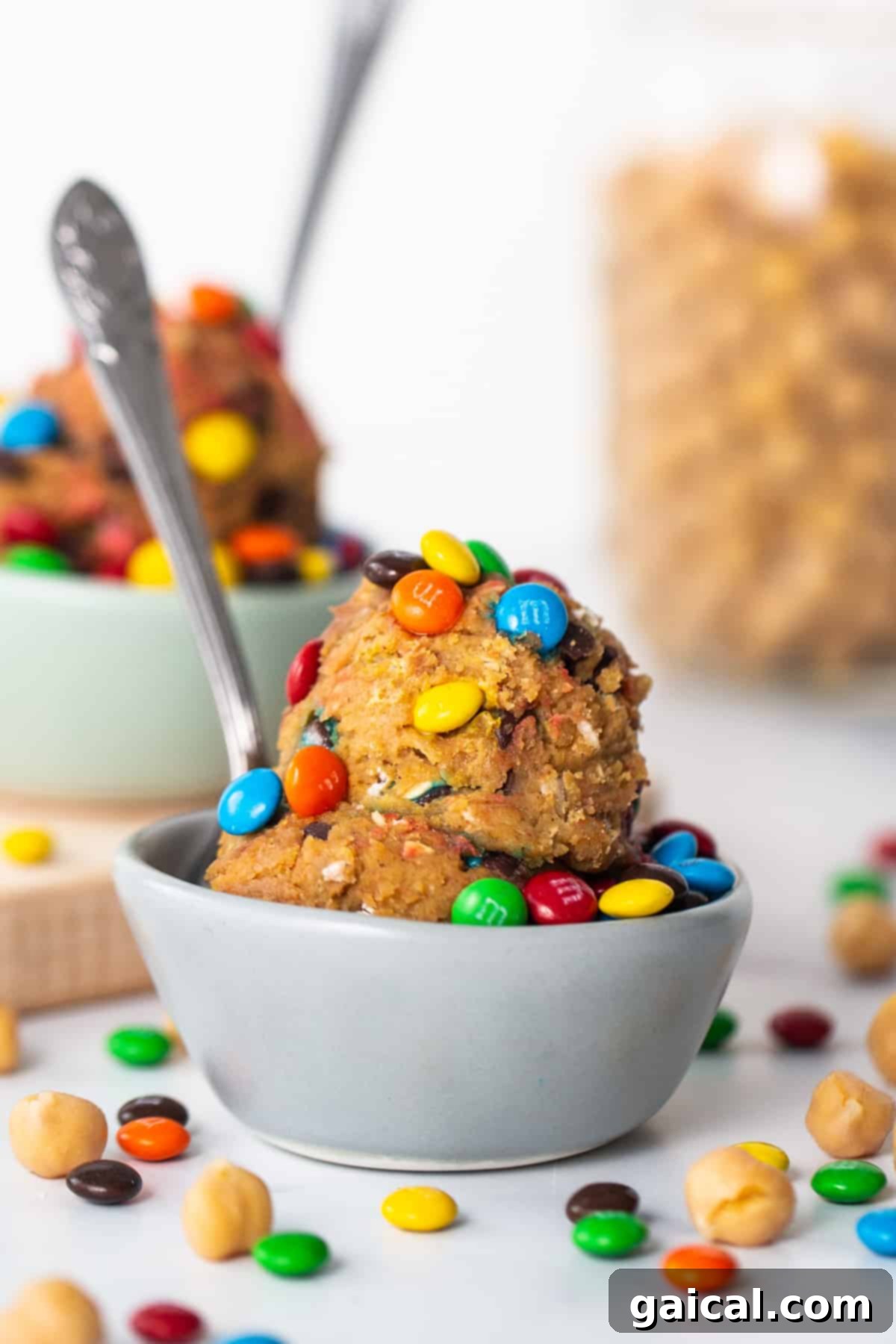 Epic Protein Cookie Dough 8 A white bowl filled with mini M&Ms and a spoon, ready to be mixed into cookie dough.