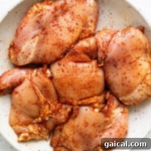 Seasoned chicken breasts on a white plate, ready for searing.