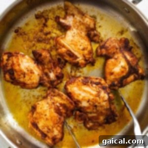 Seared chicken in a pan, being turned with two forks.