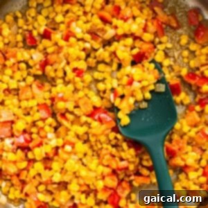 Corn and onions being sautéed in a pan with a green spatula.
