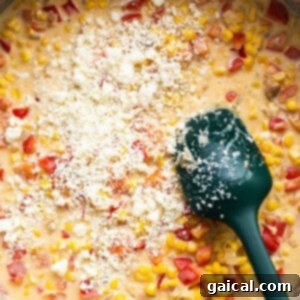 Creamy corn chowder-like sauce simmering in a pan with a green spatula.