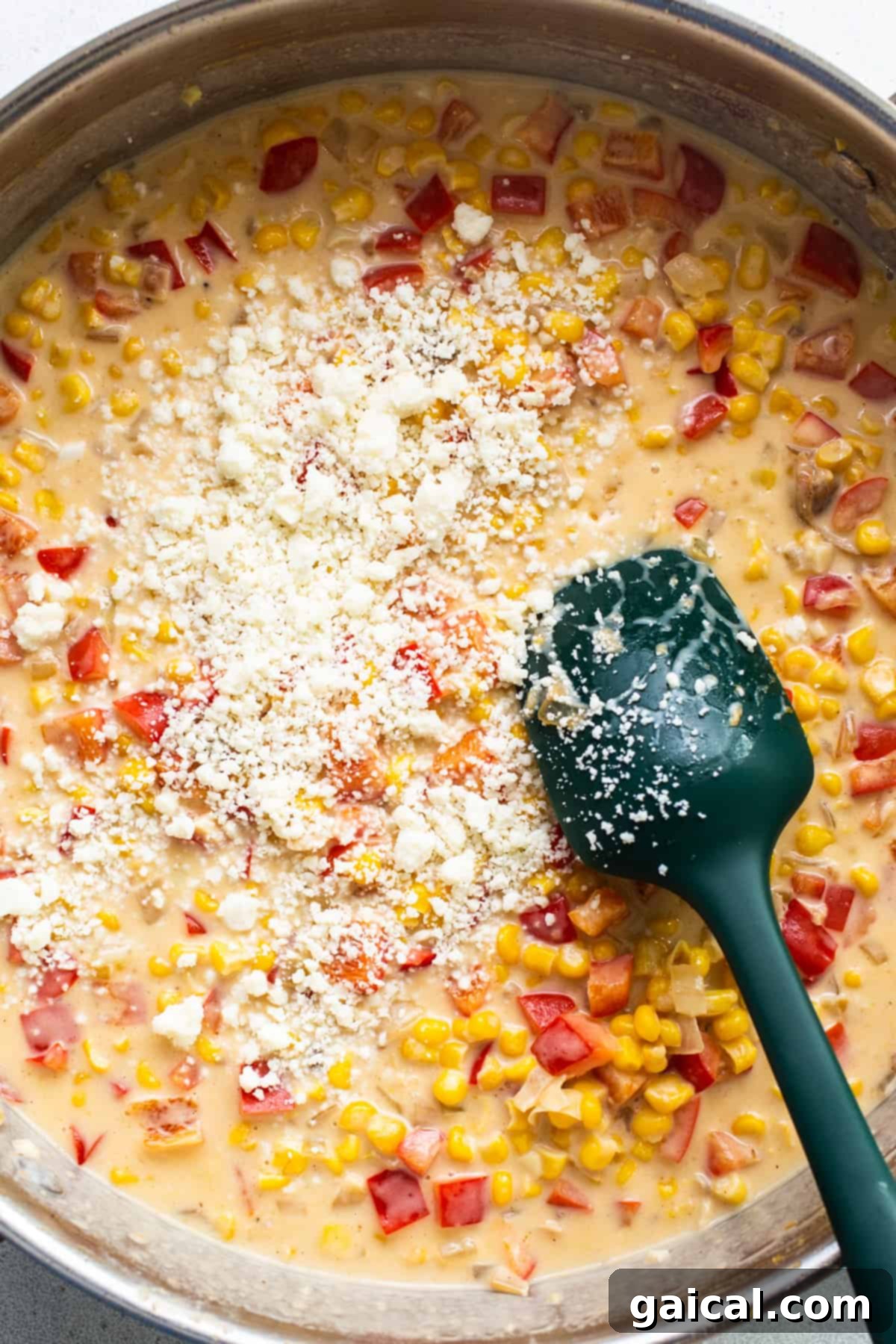 Creamy corn chowder or sauce simmering in a pan with a green spatula, waiting for chicken to be added.