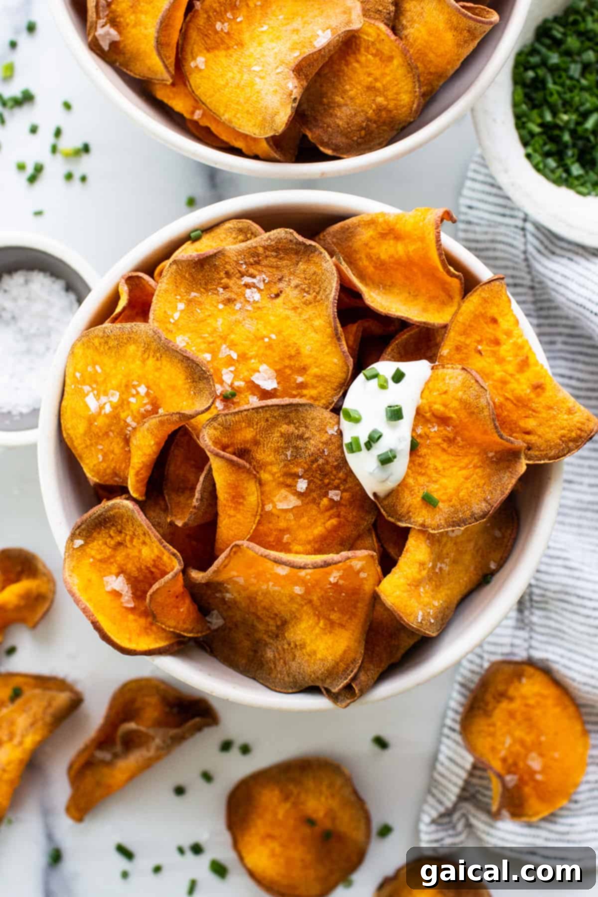 A vibrant bowl of golden crispy air fryer sweet potato chips, garnished with fresh sour cream and finely chopped chives, ready to be enjoyed.
