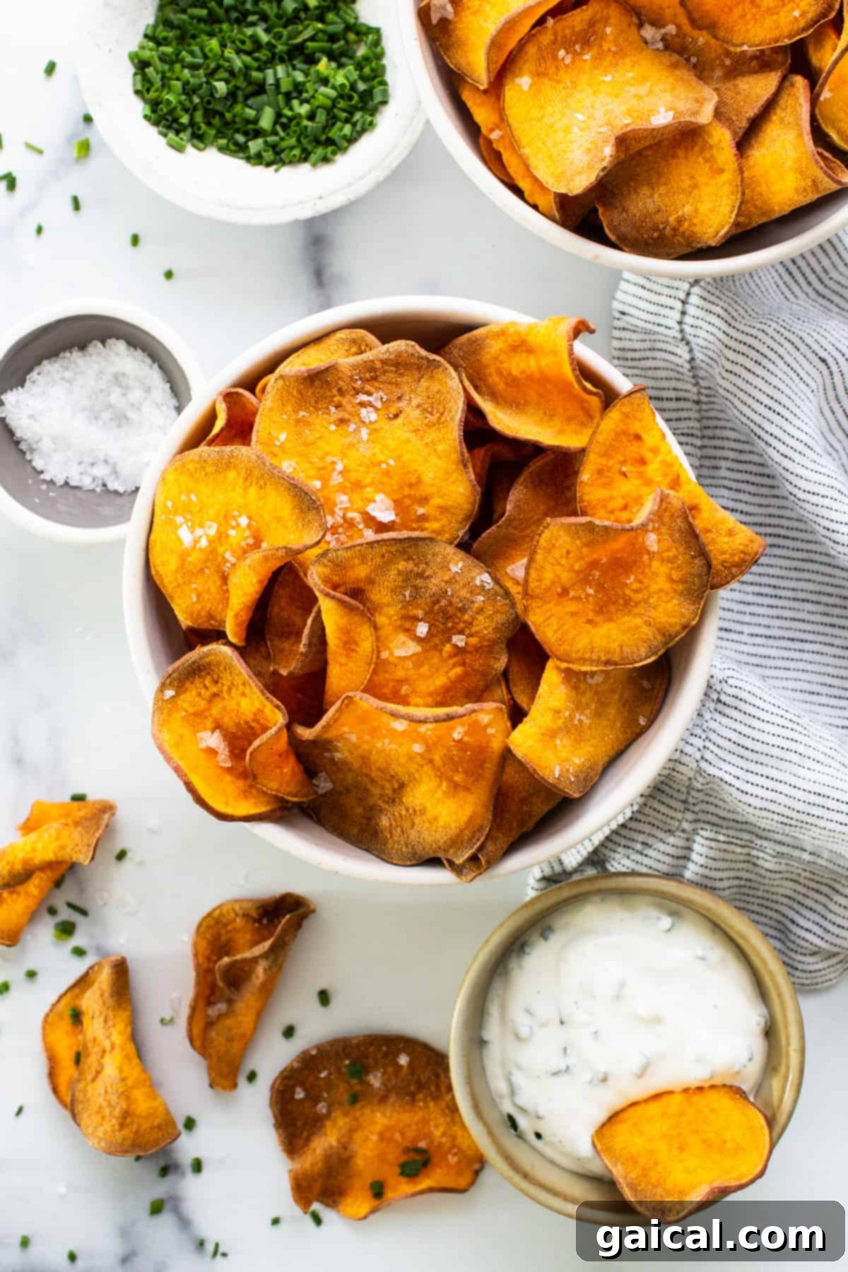A rustic wooden bowl filled with crispy sweet potato chips, accompanied by a small ramekin of creamy dipping sauce, perfectly arranged for a snack.