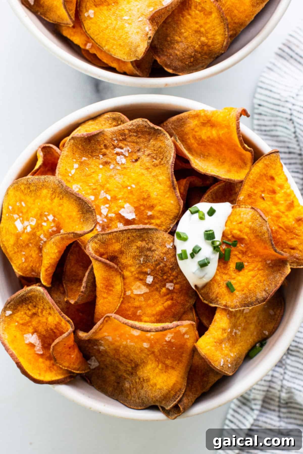 Two enticing bowls of crispy sweet potato chips, generously topped with sour cream and fresh chives, presented beautifully on a surface.