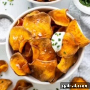 Crispy sweet potato chips served in a bowl, accompanied by a small dish of sour cream and a sprinkle of fresh parsley.