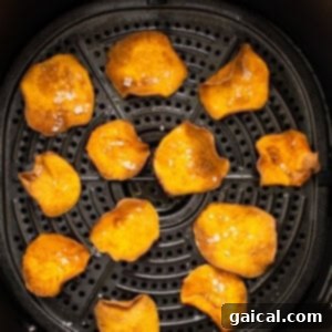 Air fryer basket filled with sweet potato chips, midway through cooking, being tossed for even crisping.