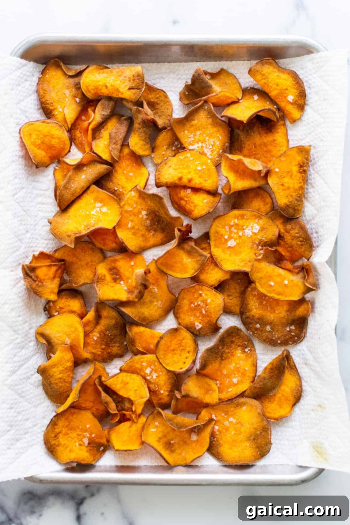 A golden batch of air-fried sweet potato chips spread out on a baking sheet, showcasing their perfect crispiness.